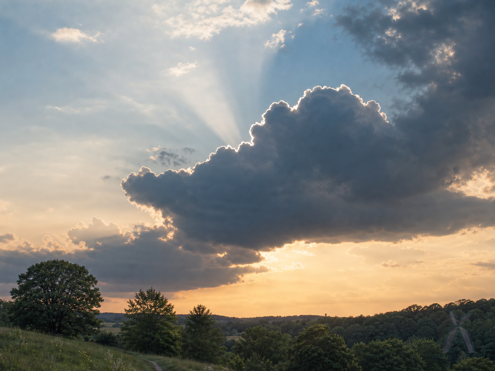 A dark cloud with a bright silver edge glowing after rain over a wide landscape.